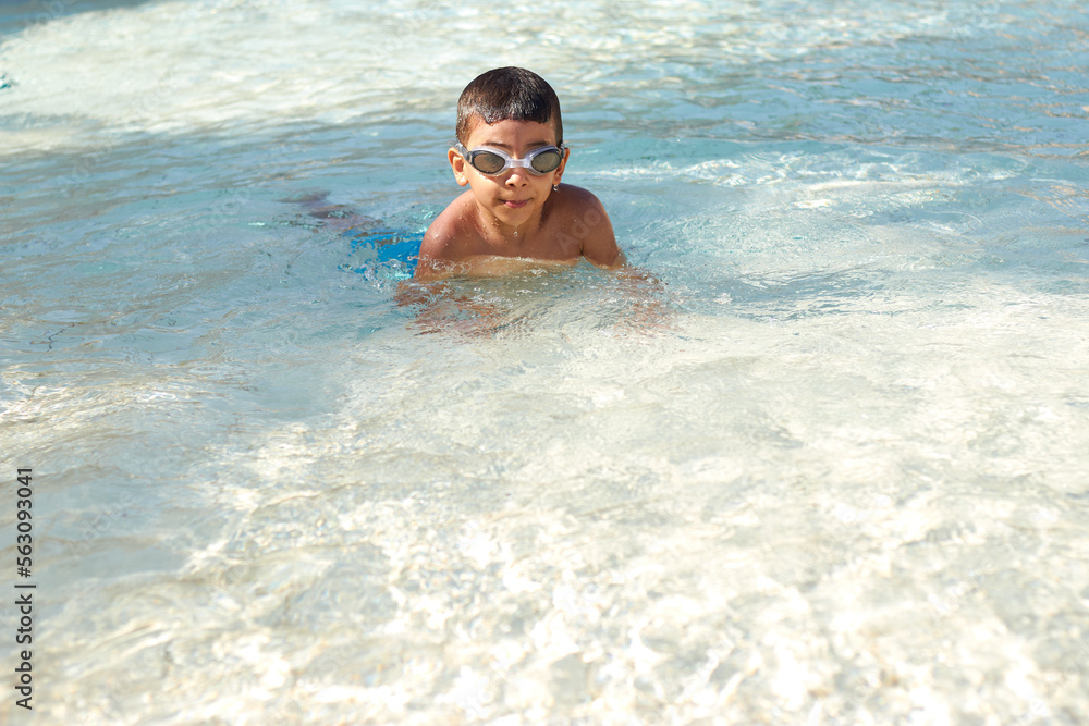 Young boy kid child six years old splashing in swimming pool having fun leisure activity wearing sea glasses practicing swimming