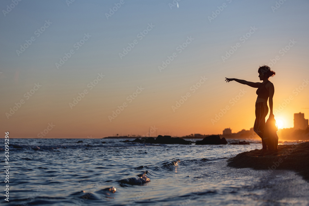 woman pointing the horizon on the beach at sunset with the city in the background