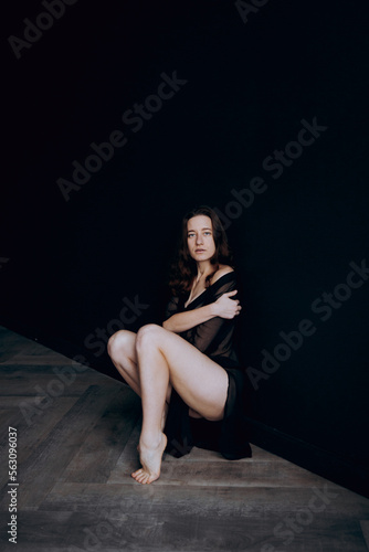 Beautiful, natural naked girl artistic posing at a stylish and fashionable nude photo shoot as a model in a photo studio with a transparent cape and bandage and looks like art