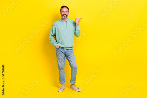 Full length photo of cheerful attractive man arm direct empty space cool proposition low price clothes isolated on yellow color background