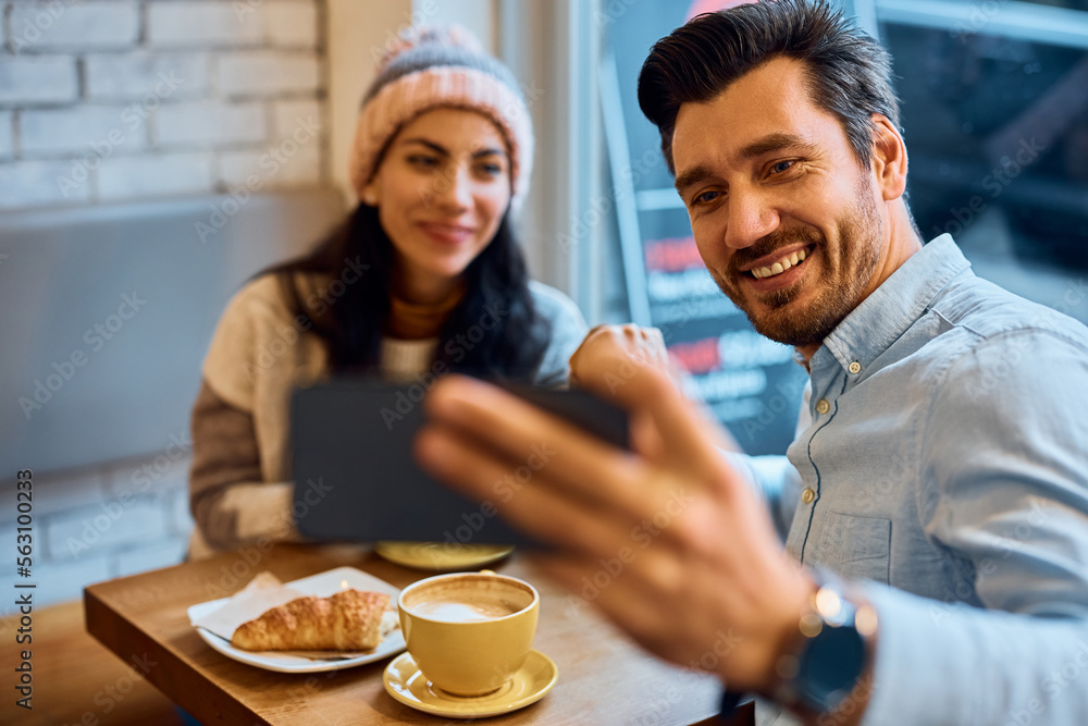 Happy man using mobile phone while taking selfie with his girlfriend in cafe. Happy man using mobile phone while taking selfie with his girlfriend in cafe.