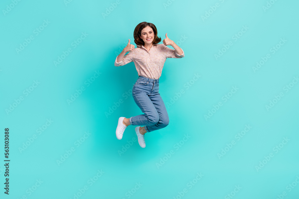 Full length photo of shiny confident lady wear pink shirt jumping hight showing two thumbs up isolated turquoise color background Full length photo of shiny confident lady wear pink shirt jumping hight showing two thumbs up isolated turquoise color background