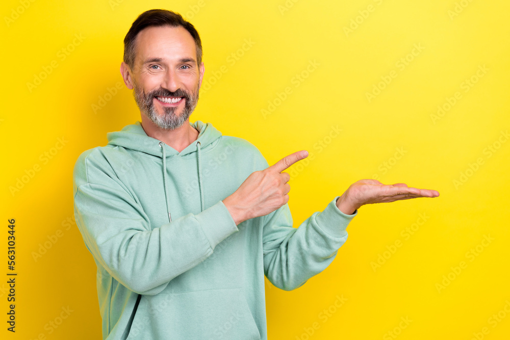 Photo of toothy beaming smiling handsome mature age man brunet hair hold palm finger point empty space object isolated on yellow color background Photo of toothy beaming smiling handsome mature age man brunet hair hold palm finger point empty space object isolated on yellow color background