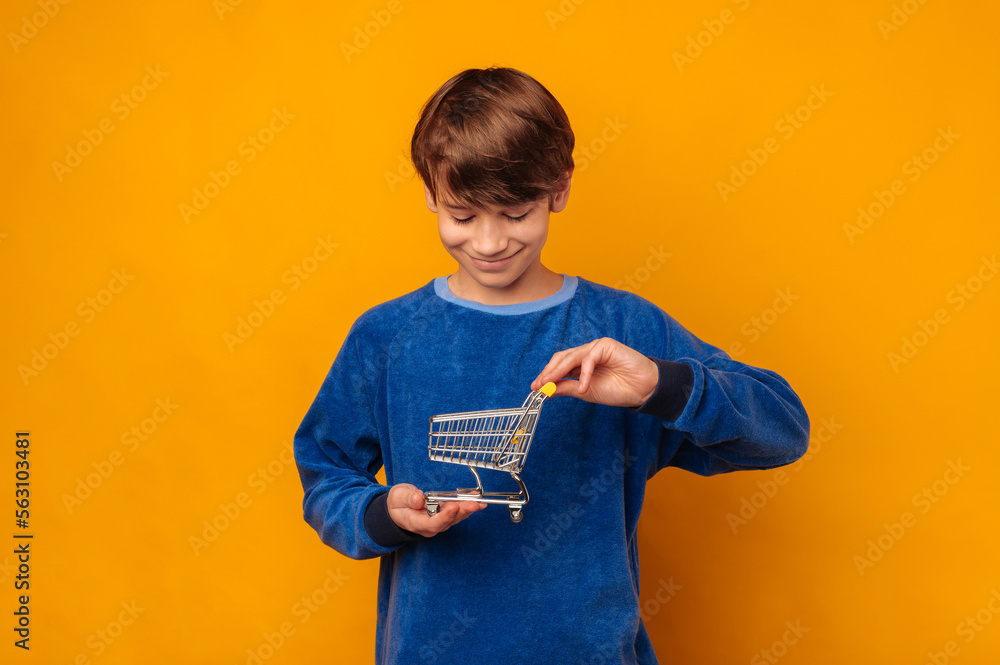 Smiling boy wants to learn about financials while holding a shopping trolley over yellow background. Smiling boy wants to learn about financials while holding a shopping trolley over yellow background.