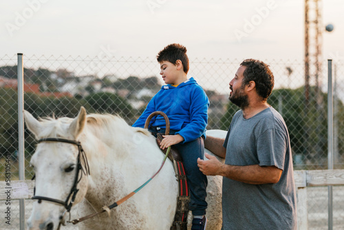 Boy with cerebral palsy riding a horse next to instructor