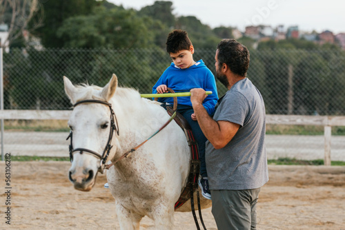 Disabled young man riding a horse assisted by an instructor