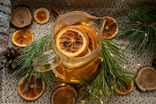 Green tea in a transparent, glass teapot. Dried oranges and Christmas tree branches