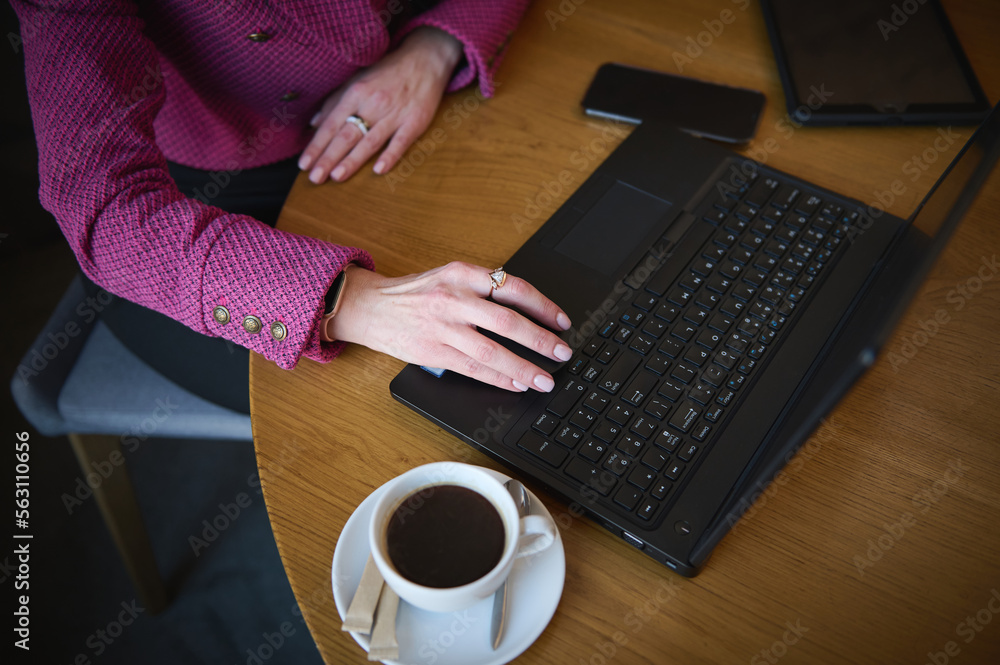 Top view of a businesswoman's hand on laptop keyboard while telecommuting from a cafeteria interior. Business on the go concept. Urban life. People. Lifestyle concept