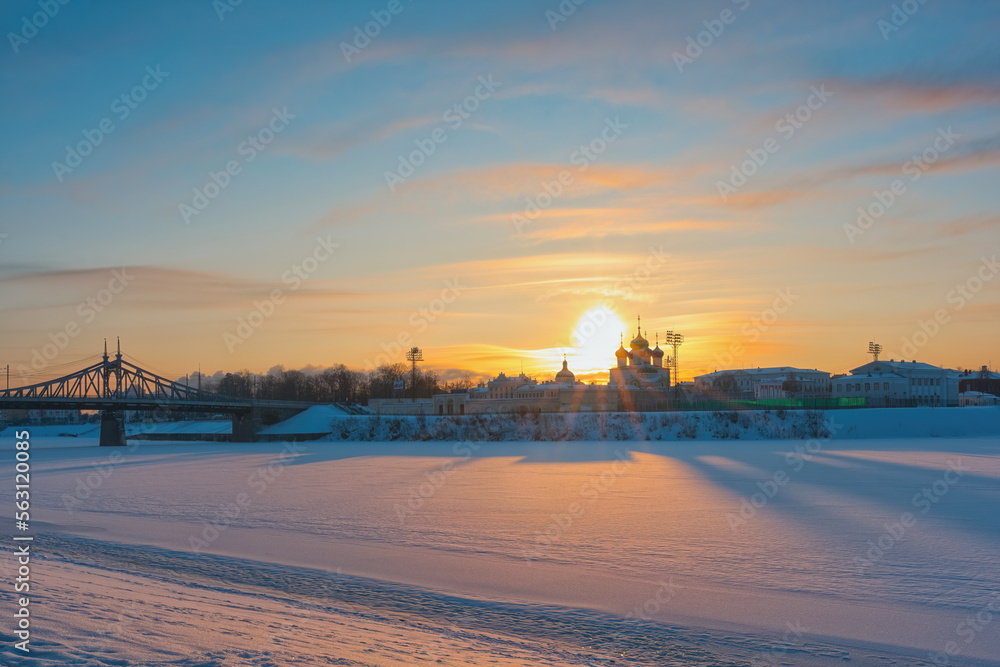 A man walks on the ice of a frozen river in the rays of the morning sun. View of the embankment of the Volga River.