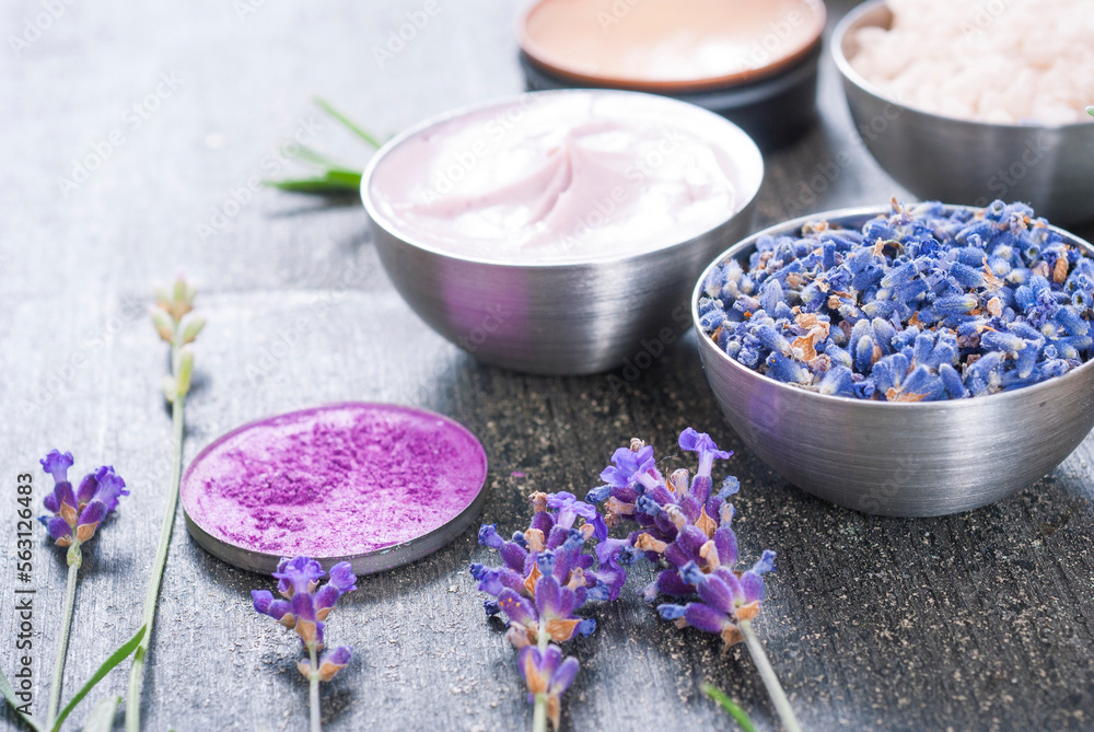 beauty product samples with fresh purple and blue dried lavenders, bath salts and massage pouches on dark wood table background beauty product samples with fresh purple and blue dried lavenders, bath salts and massage pouches on dark wood table background