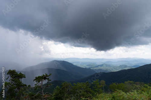 Canvas Print Sheets of rain from a very dark cloud over a mountain landscape, sunny skies in