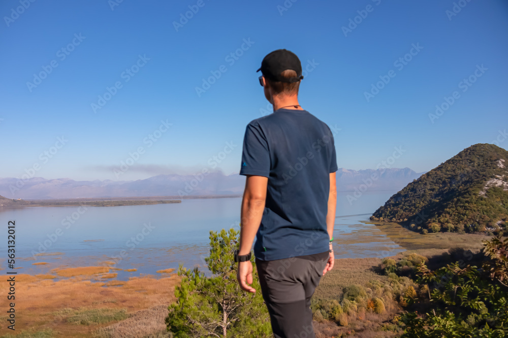 Rear view of man with panoramic view of Lake Skadar National Park in autumn seen from Virpazar, Bar, Montenegro, Balkans, Europe. Stunning travel destination in Dinaric Alps near Albanian border Rear view of man with panoramic view of Lake Skadar National Park in autumn seen from Virpazar, Bar, Montenegro, Balkans, Europe. Stunning travel destination in Dinaric Alps near Albanian border