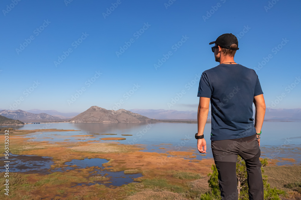 Rear view of man with panoramic view of Lake Skadar National Park in autumn seen from Virpazar, Bar, Montenegro, Balkans, Europe. Stunning travel destination in Dinaric Alps near Albanian border