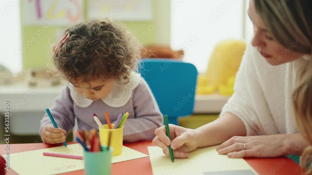 Teacher and toddler sitting on table drawing on paper at kindergarten Teacher and toddler sitting on table drawing on paper at kindergarten