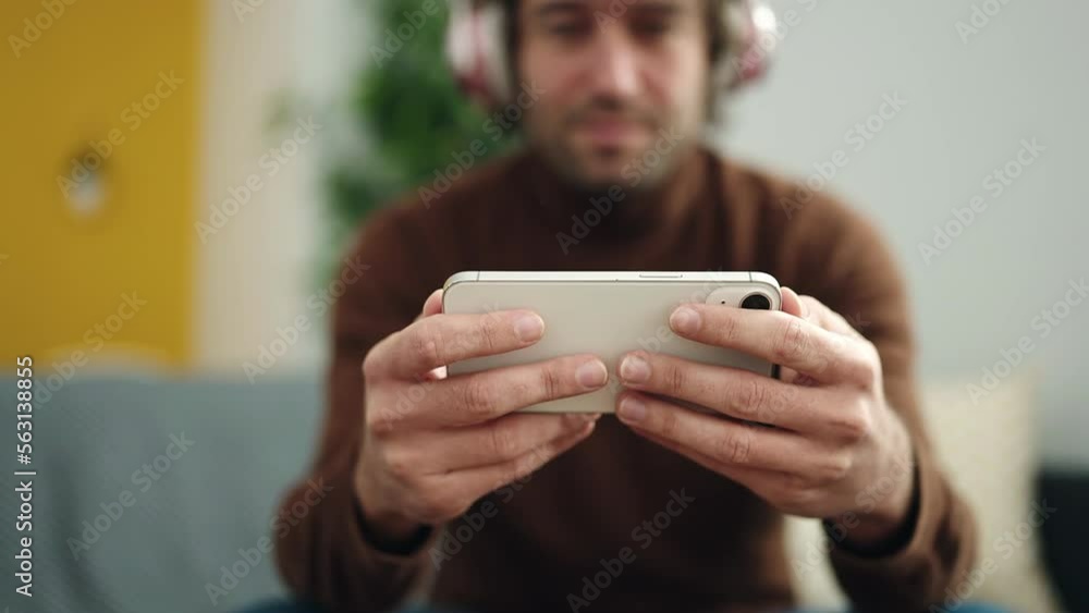 Young hispanic man watching video on smartphone sitting on sofa at home Young hispanic man watching video on smartphone sitting on sofa at home