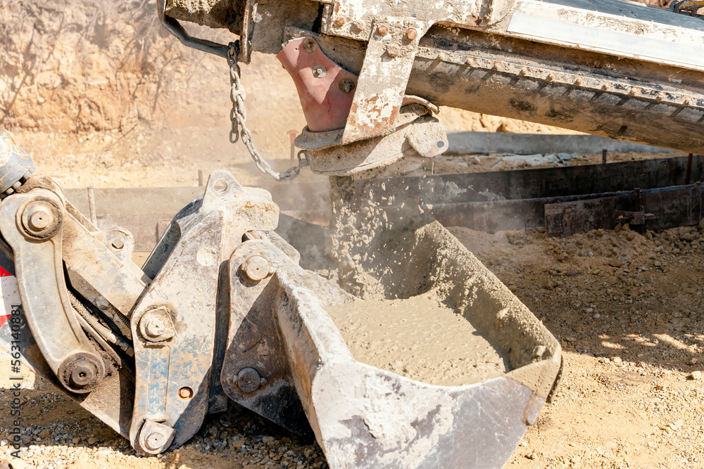 Concrete mixer truck pouring fresh wet concrete into excavators bucket at a construction site Concrete mixer truck pouring fresh wet concrete into excavators bucket at a construction site