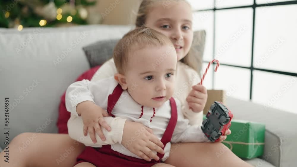 Brother and sister hugging each other sitting on sofa by christmas tree at home Brother and sister hugging each other sitting on sofa by christmas tree at home