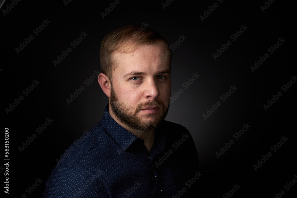 Portrait of a young confident blonde in a dark shirt, with a beard on a dark background Portrait of a young confident blonde in a dark shirt, with a beard on a dark background