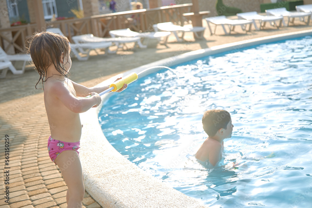 Positive children splash water in the pool in summer.