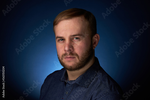 Portrait of a young confident blonde in a dark shirt, with a beard on a dark background