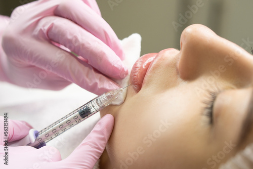 Lip augmentation and correction procedure in a cosmetology salon. The specialist makes an injection in the patient lips.