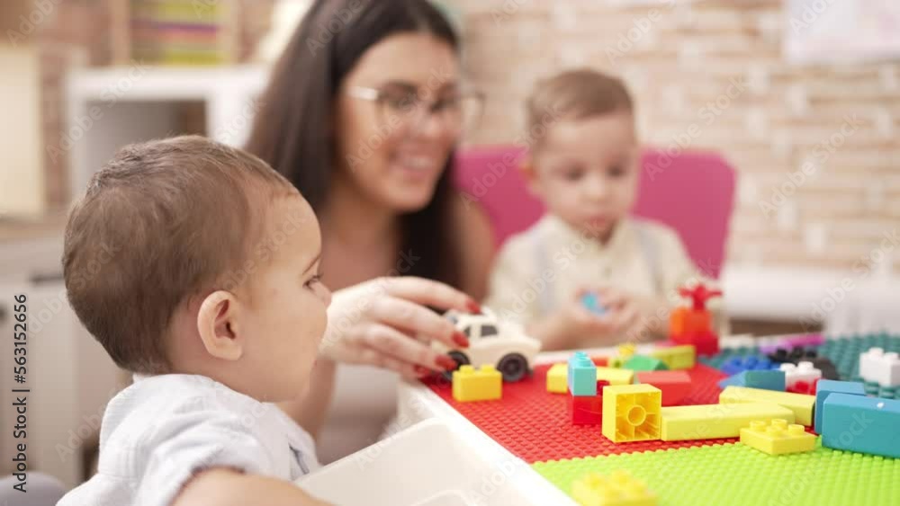 Teacher with boys playing with construction blocks sitting on table at kindergarten Teacher with boys playing with construction blocks sitting on table at kindergarten