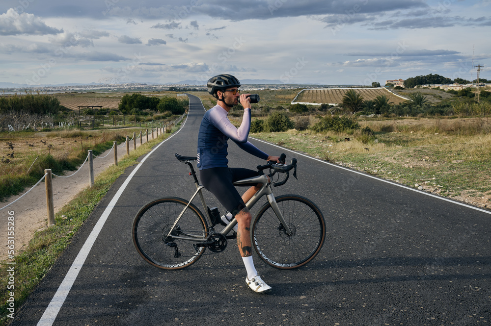 Male cyclist on a gravel bike drinks water during exercise.Empty city road.
Sports motivation.Murcia region in Spain