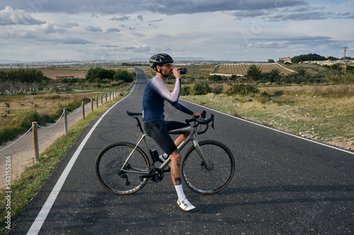 Male cyclist on a gravel bike drinks water during exercise.Empty city road. Sports motivation.Murcia region in Spain