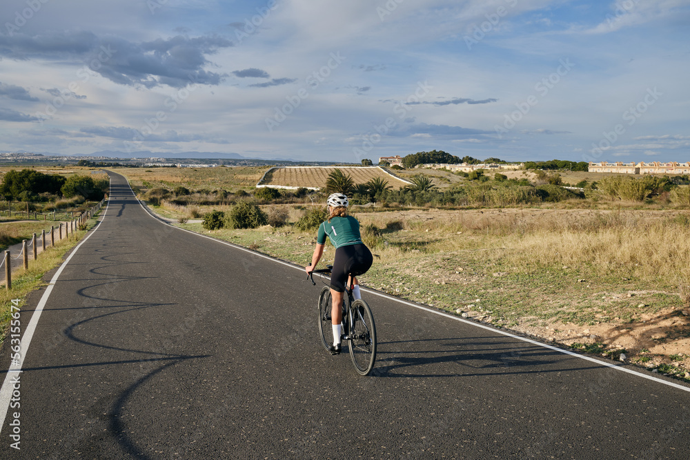 Obraz premium fit young female cyclist riding on the road on a gravel bike at sunset.Empty city road. Sports motivation.Murcia region in Spain