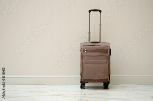 A brown suitcase on wheels stands against the beige wall. Travel and vacation concept. Bag for things of the tourist. Luggage at the airport or hotel.