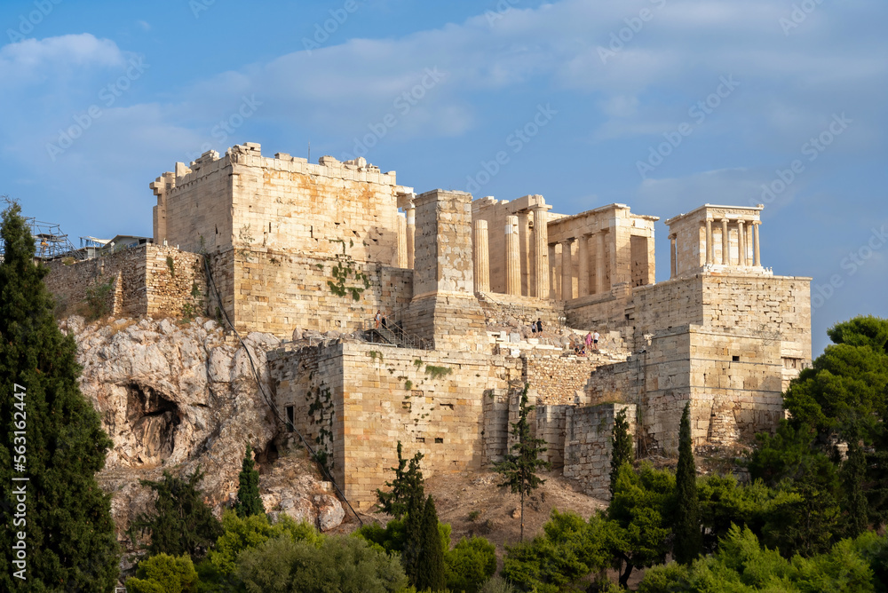 The Acropolis of Athens as seen from the Areopagus Hill in Plaka district. The Propylaea (monumental gateway to the Acropolis), temple of the Athena Nike on the right. Sunny day, cloudy blue sky