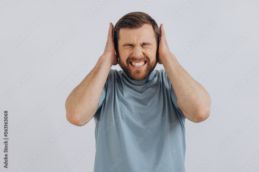 Portrait of a modern bearded middle-aged man in a blue t-shirt showing emotions covering his ears on a white background Portrait of a modern bearded middle-aged man in a blue t-shirt showing emotions covering his ears on a white background