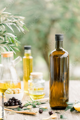 Fototapeta Naklejka Na Ścianę i Meble -  Olive oil bottle and olive oil in glass on old wooden table under olive tree.