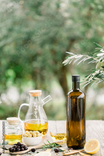 Olive oil bottle and olive oil in glass on old wooden table under olive tree.