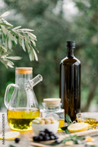 Olive oil bottle and olive oil in glass on old wooden table under olive tree.