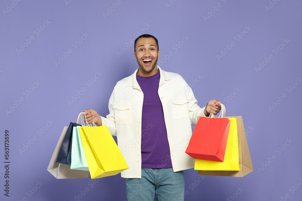 Happy African American man with shopping bags on purple background Happy African American man with shopping bags on purple background
