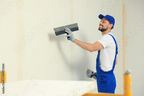 Professional worker plastering wall with putty knives indoors. Space for text photo