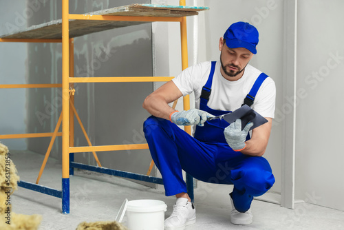 Professional worker putting plaster on putty knife indoors photo