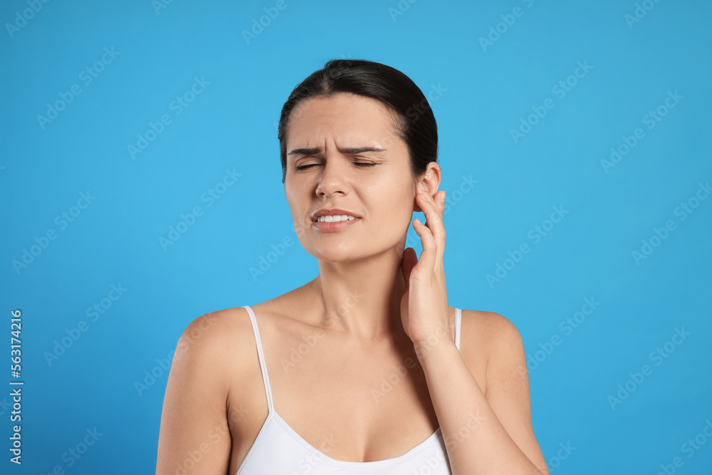 Young woman suffering from ear pain on light blue background Young woman suffering from ear pain on light blue background