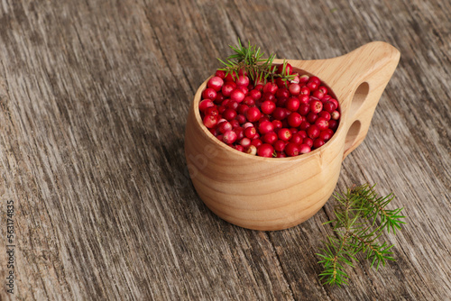 Cup with tasty ripe lingonberries and spruce twigs on wooden surface, space for text