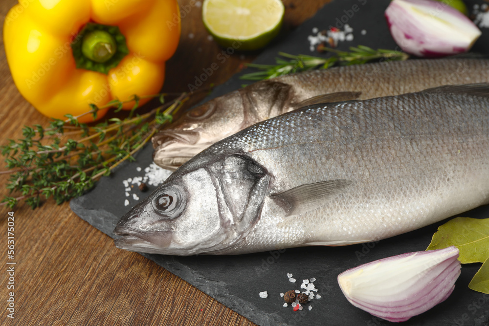 Sea bass fish and ingredients on wooden table, closeup