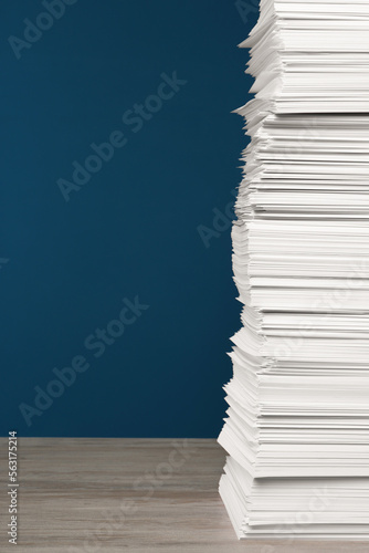 Stack of white paper sheets on wooden table against blue background  space copy text