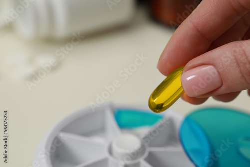 Woman taking pill from plastic box at white table  closeup. Space for text