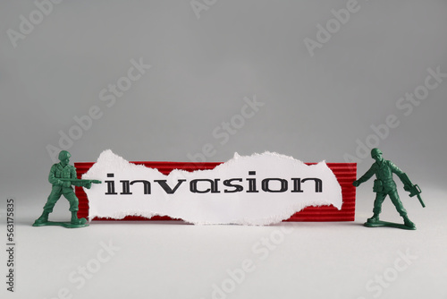 Paper with word Invasion and toy soldiers on light grey background photo