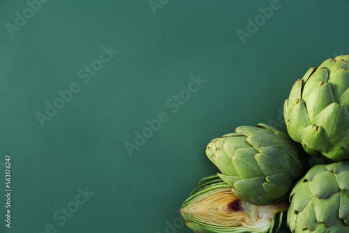 Cut and whole fresh raw artichokes on green background, flat lay. Space for text