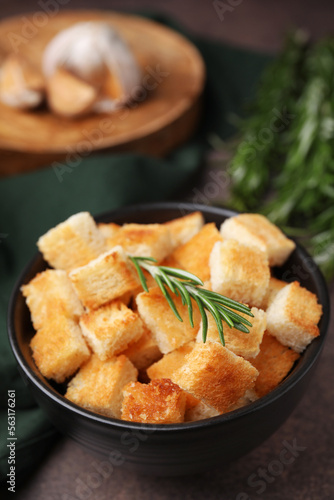 Delicious crispy croutons and rosemary in bowl on dark table, closeup