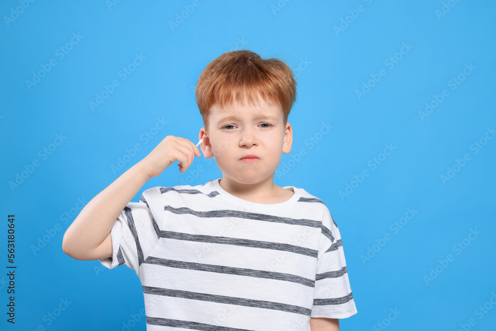 Little boy cleaning ear with cotton swab on light blue background Little boy cleaning ear with cotton swab on light blue background