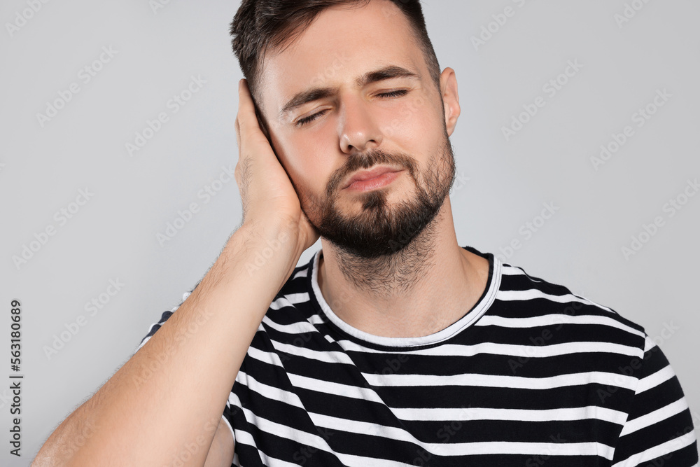 Fototapeta premium Young man suffering from ear pain on light grey background