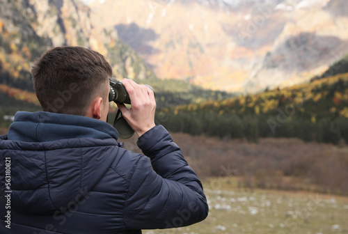 Boy looking through binoculars in beautiful mountains, back view. Space for text