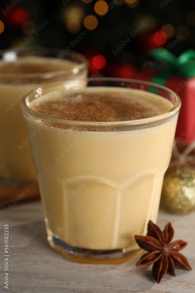 Tasty eggnog with cinnamon and anise on white wooden table against blurred festive lights, closeup Tasty eggnog with cinnamon and anise on white wooden table against blurred festive lights, closeup